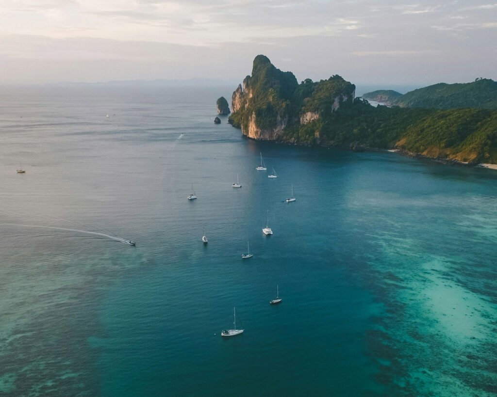 Aerial view of a tropical coastline with lush green islands and turquoise waters dotted with several boats.